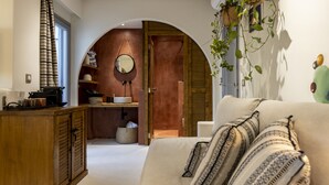 Una habitación acogedora con un armario de madera, un sofá con cojines estampados, un espejo y vistas a una cocina.