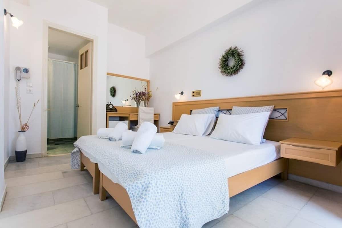 Habitación de hotel con una cama grande, una mesita de noche, un espejo, una lámpara de pared y una puerta que da al baño.
