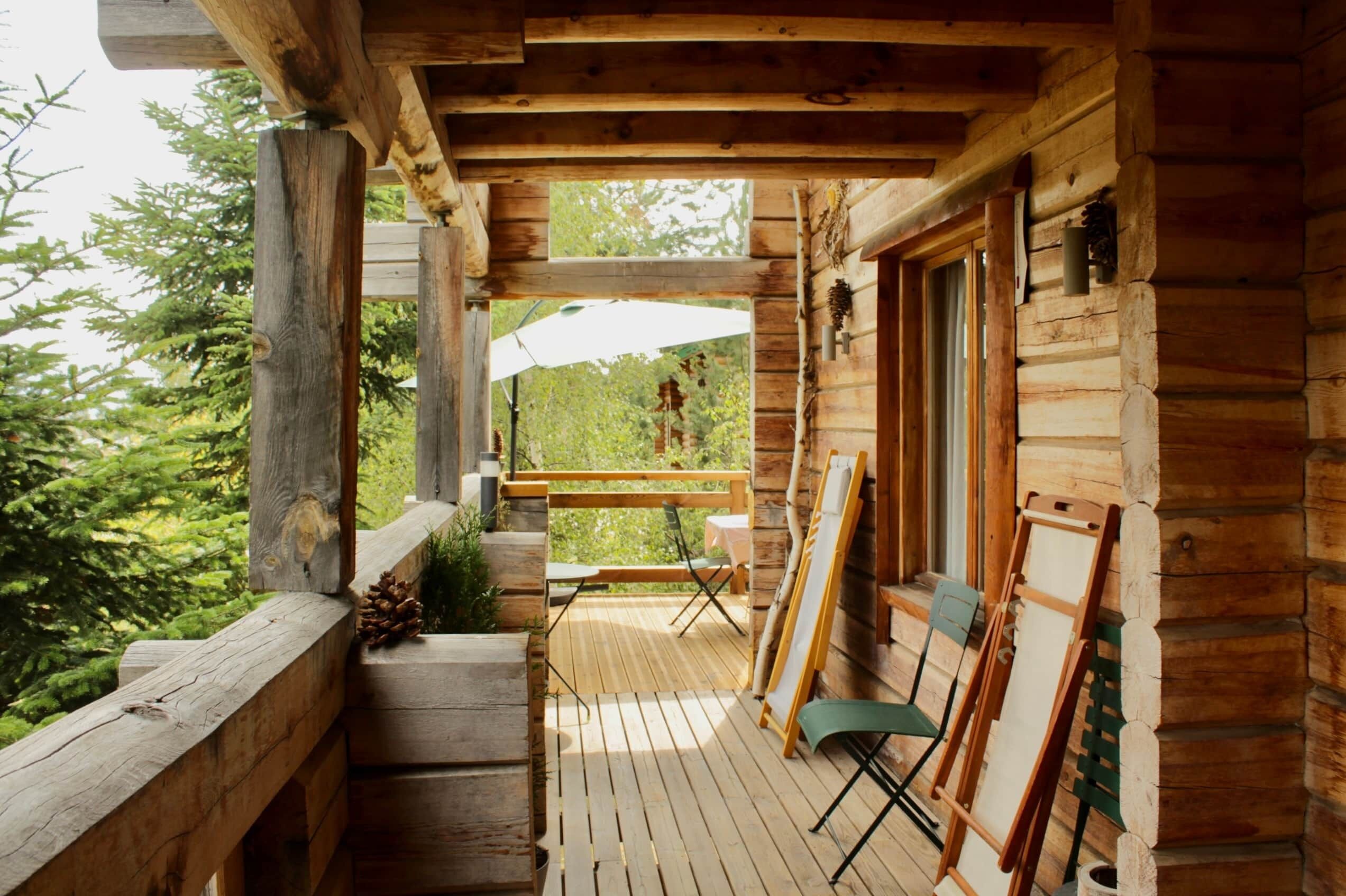 En træterrasse med et bord og stole, et gelænder af træ og udsigt til træer.