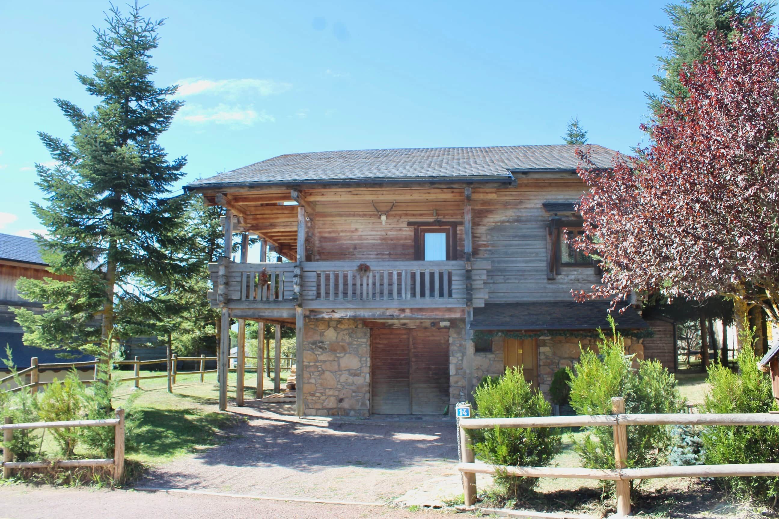 Una cabaña de madera con balcón, cimientos de piedra y un patio cercado.