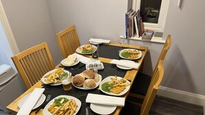 A dining table set with various dishes, including fries, burgers, and bread, in a room with wooden chairs and a window with magazines on the sill. - Blaydonburn - Sleeps 4,5 - Parking - Hottub - Yard (Blaydon on Tyne)