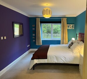 Um quarto com cama, janela com cortinas, luminária na parede e um quadro.