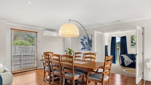 Un comedor con una mesa y sillas de madera, una lámpara colgante y vistas al exterior a través de una ventana con persianas.
