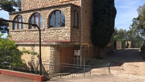 A stone building with a tiled roof, arched windows, and a fenced driveway. - Maison en Pierres Avec vue sur mer et les Îles (Bormes-les-Mimosas)