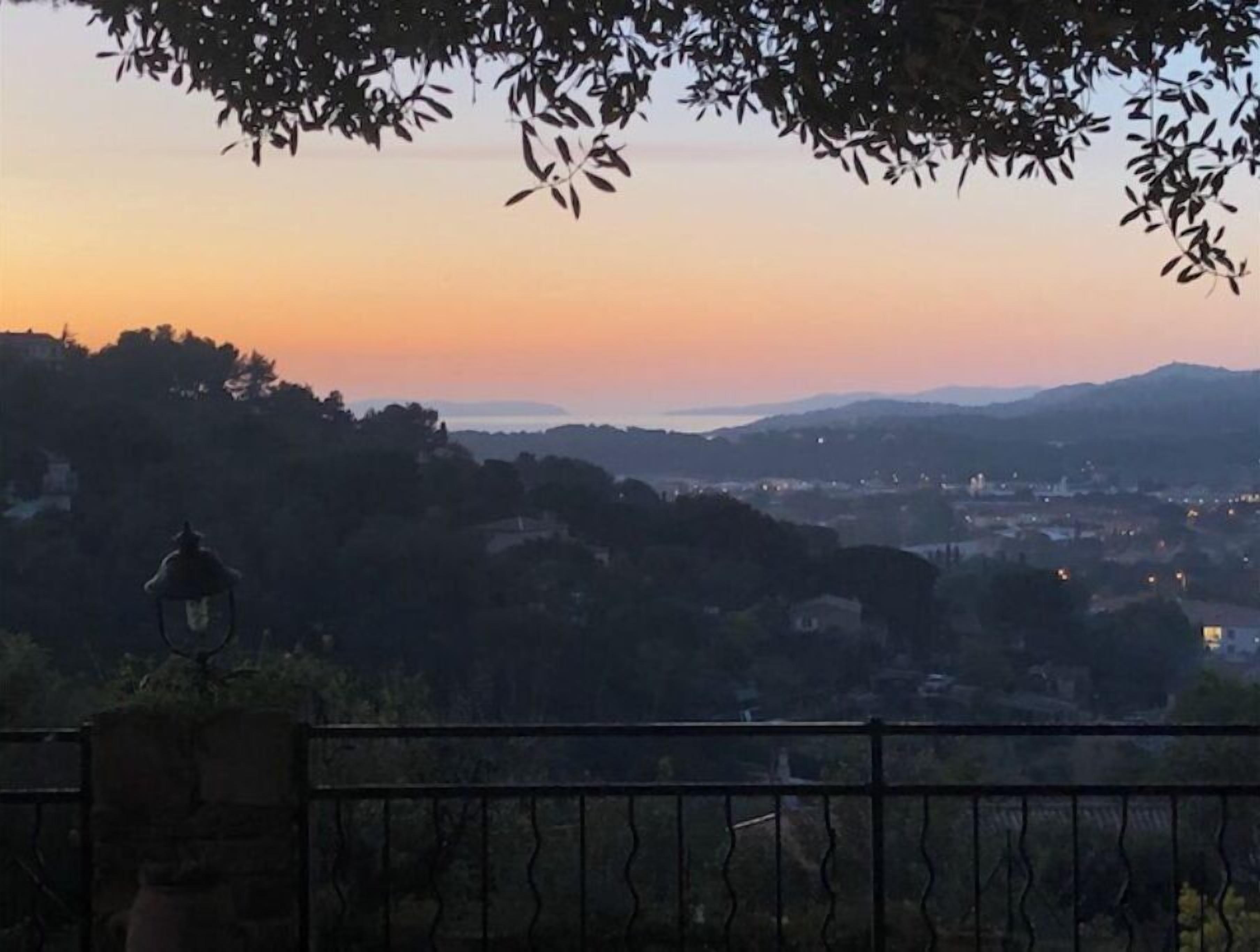Ein weiter Panoramablick auf eine Stadt in der Dämmerung, mit klarem Himmel, fernen Bergen und einem Gewässer.