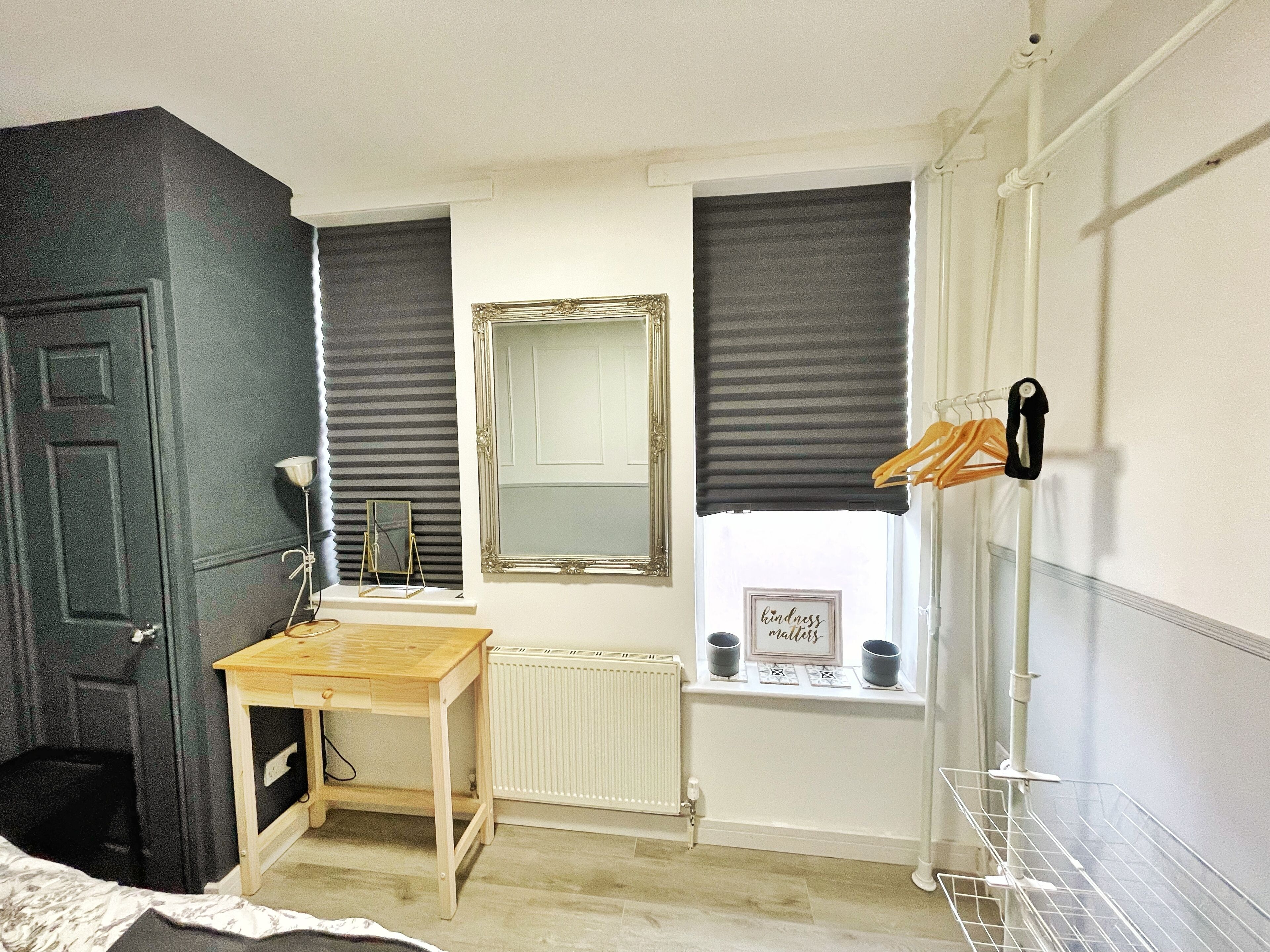 A small bedroom with a bed, a desk, a mirror, and a radiator.