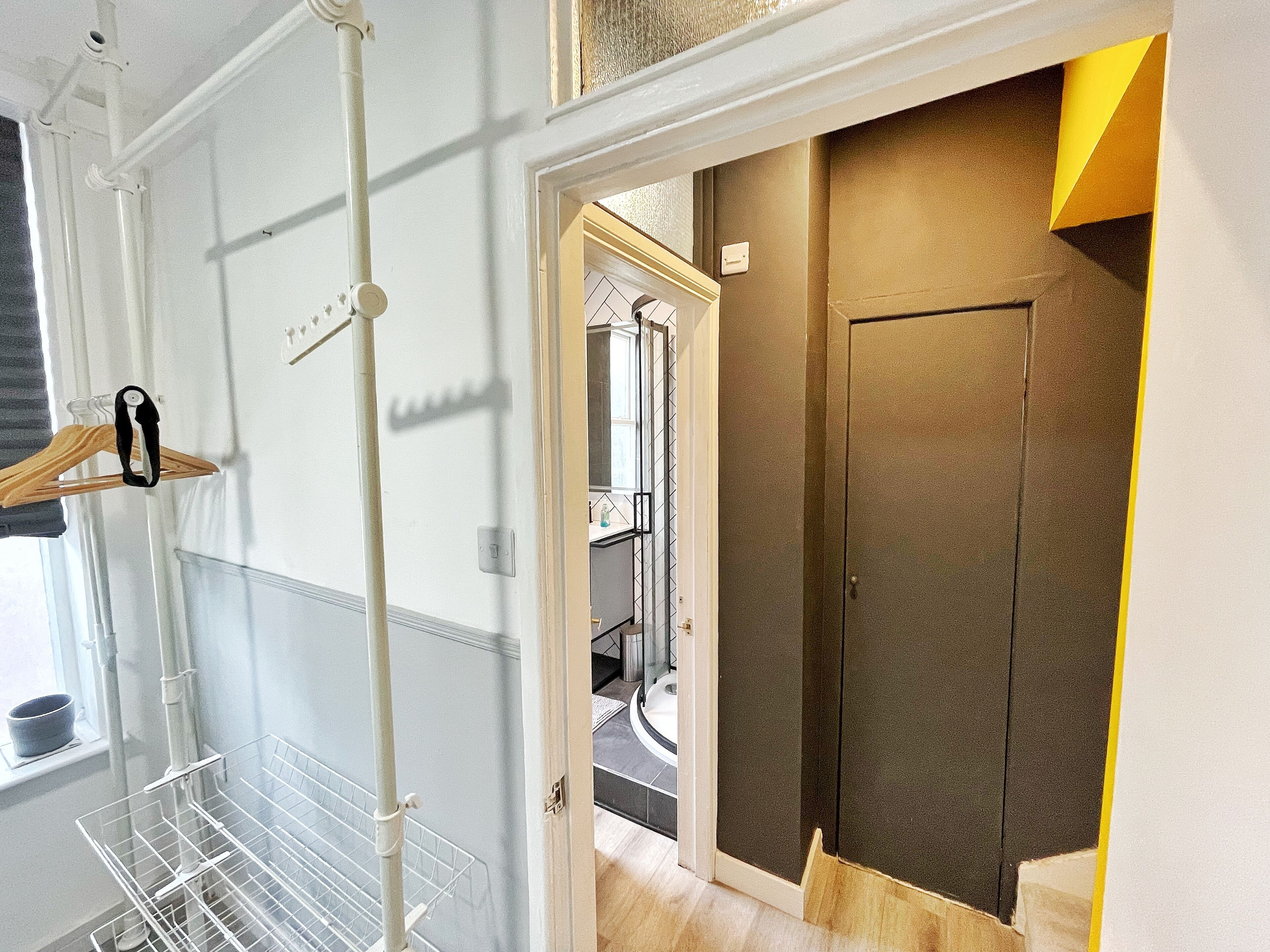 A hallway with a white metal rack, a door with a yellow accent, and a glimpse of a bathroom with a tiled wall.