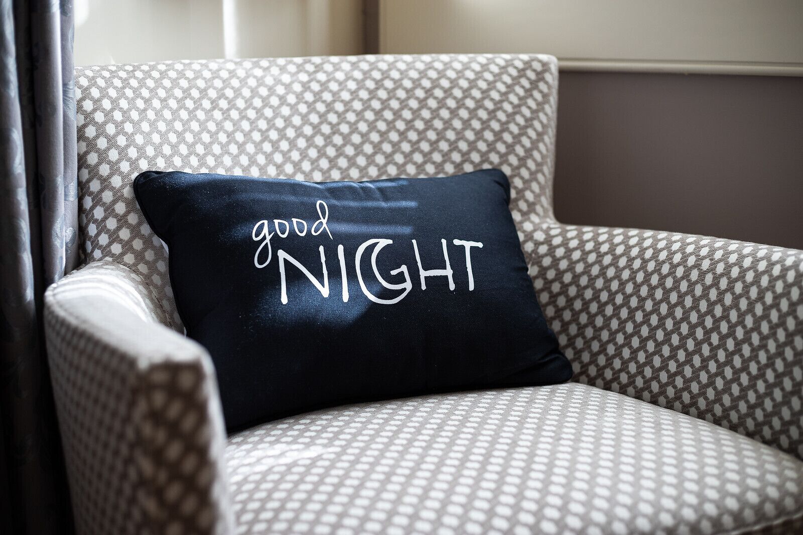 A chair with a patterned fabric and a black pillow with the words "good NIGHT" written on it.