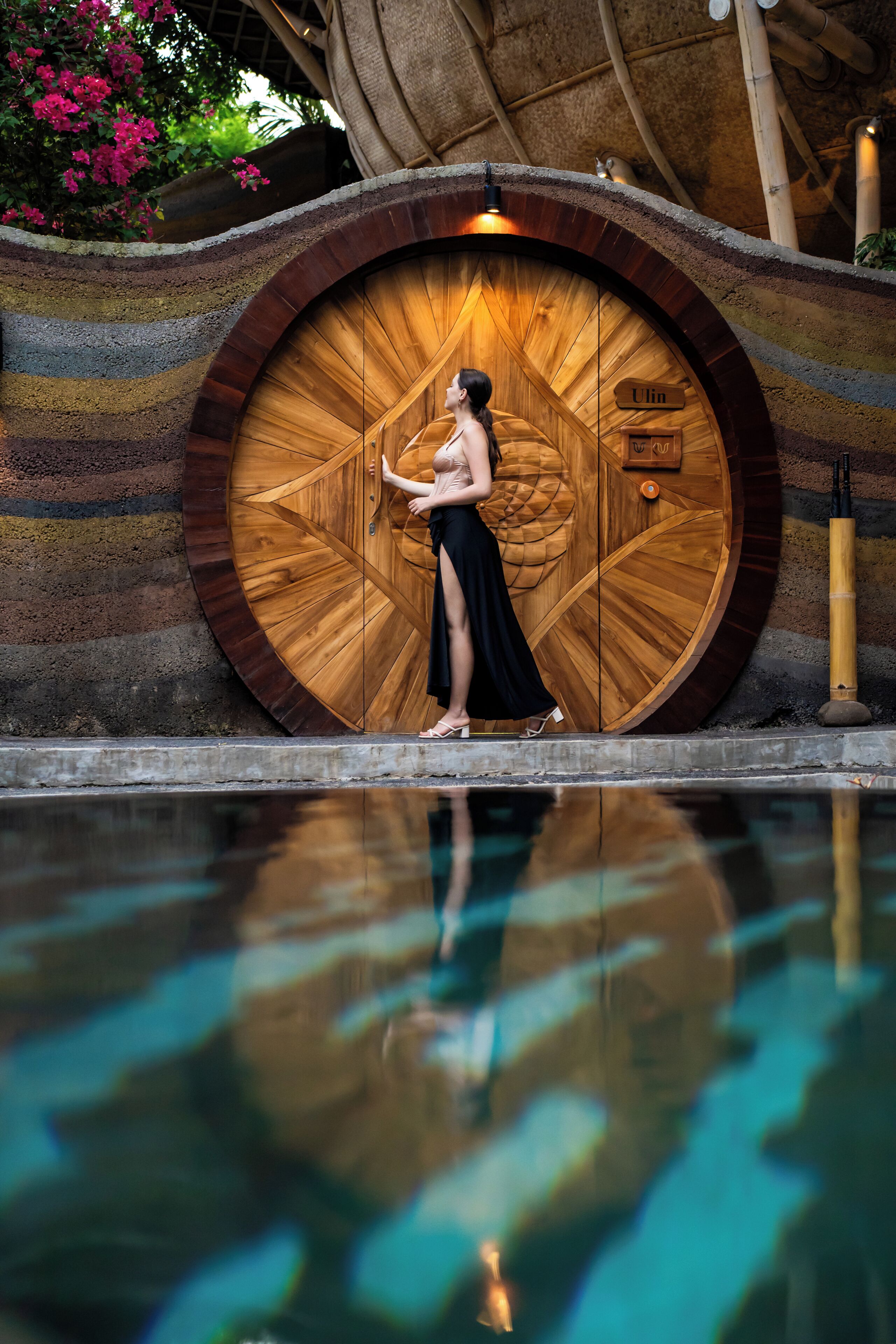 A woman standing by a large wooden door with a sign reading 'Ulin.'