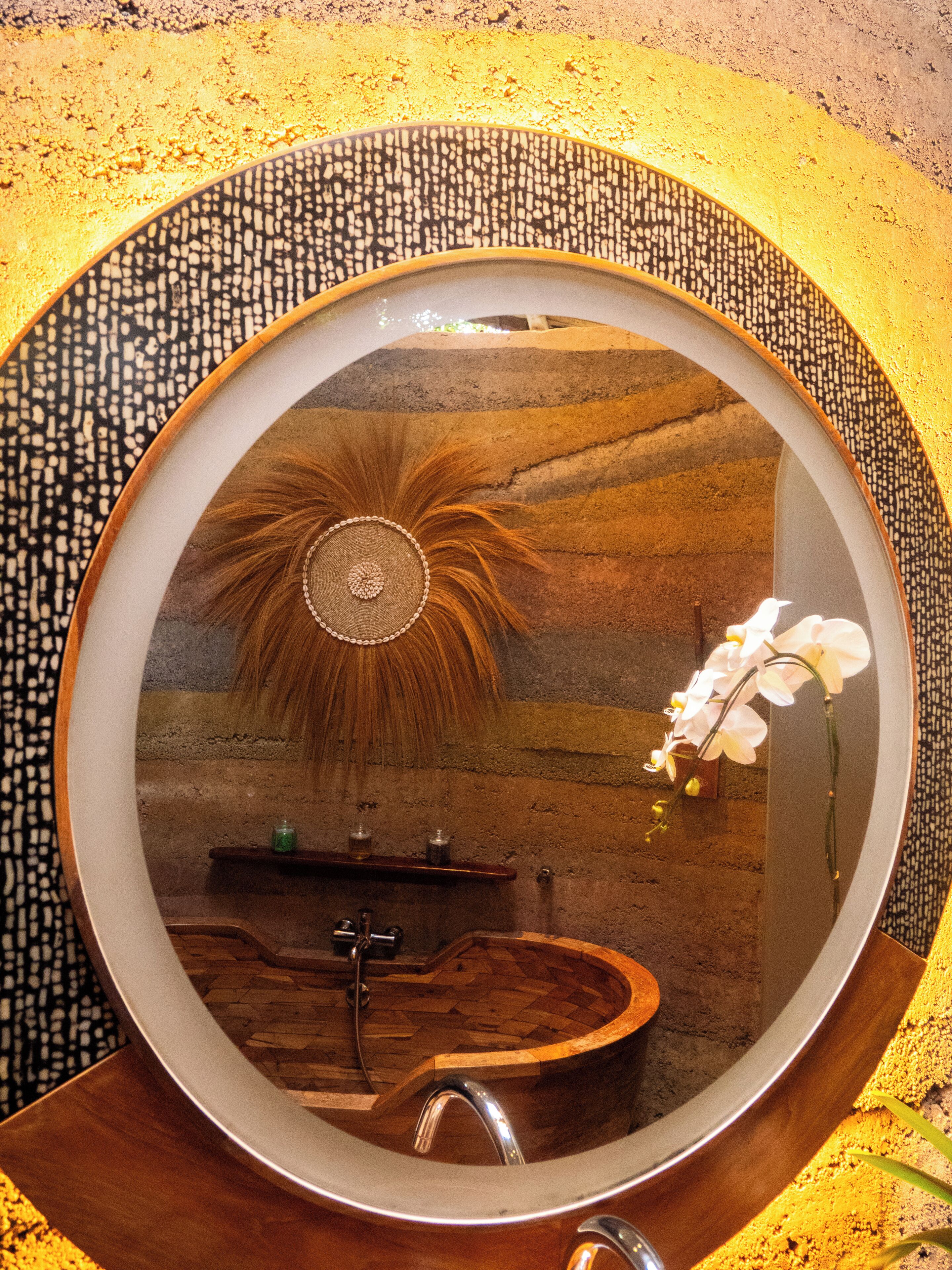 A bathroom with a round mirror, a wooden bathtub, and a sink.