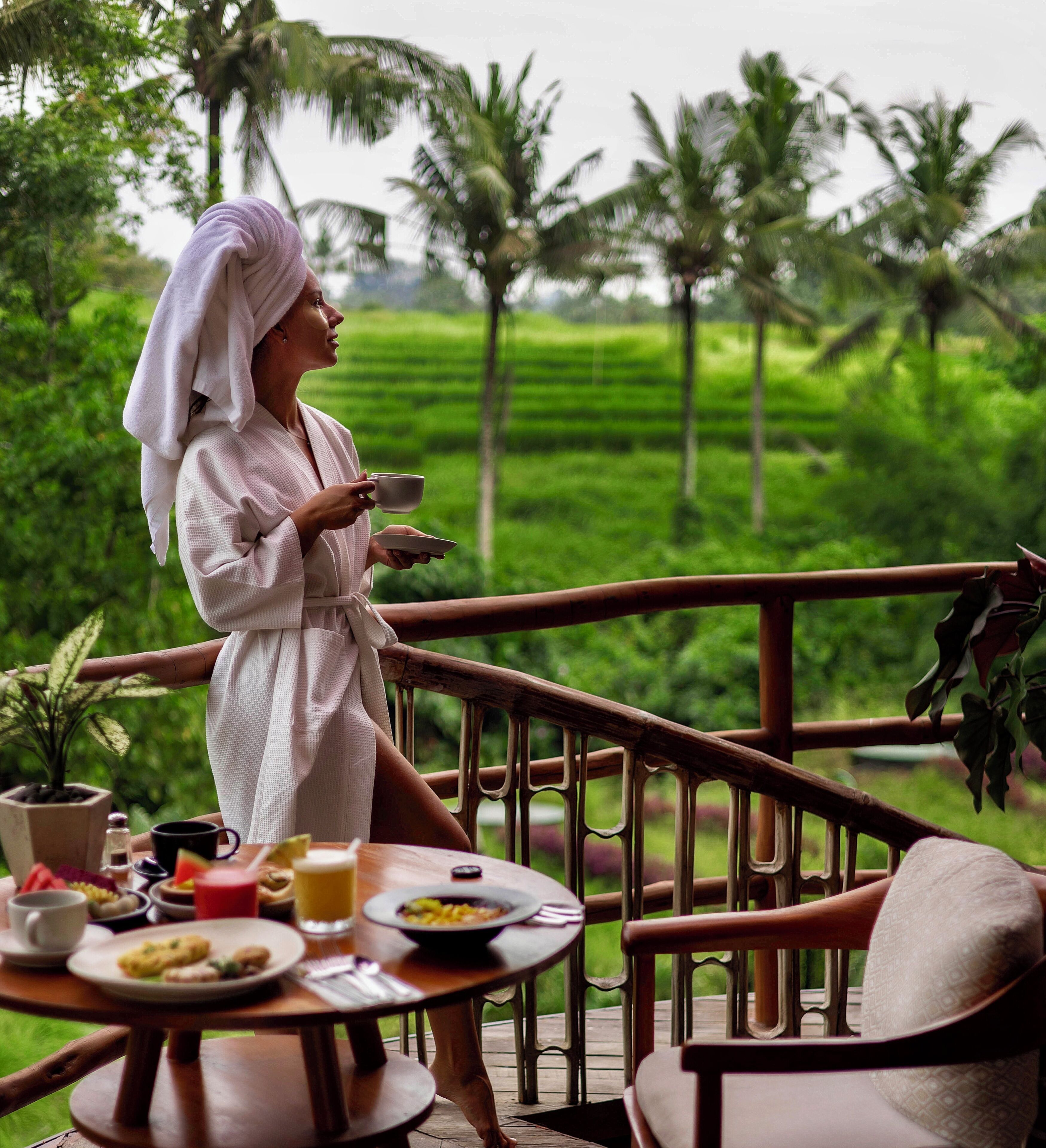 A person in a white robe sitting at a wooden table with a view of a lush green landscape.