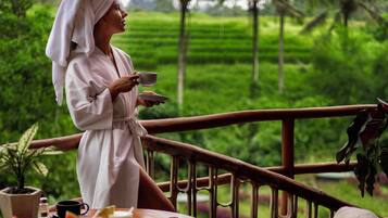 A person in a white robe sitting at a wooden table with a view of a lush green landscape.