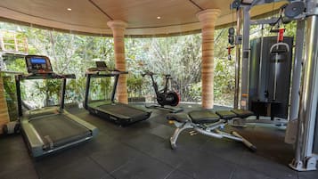 Un gimnasio con cintas de correr, elípticas y máquinas de pesas, rodeado de amplias ventanas y columnas.