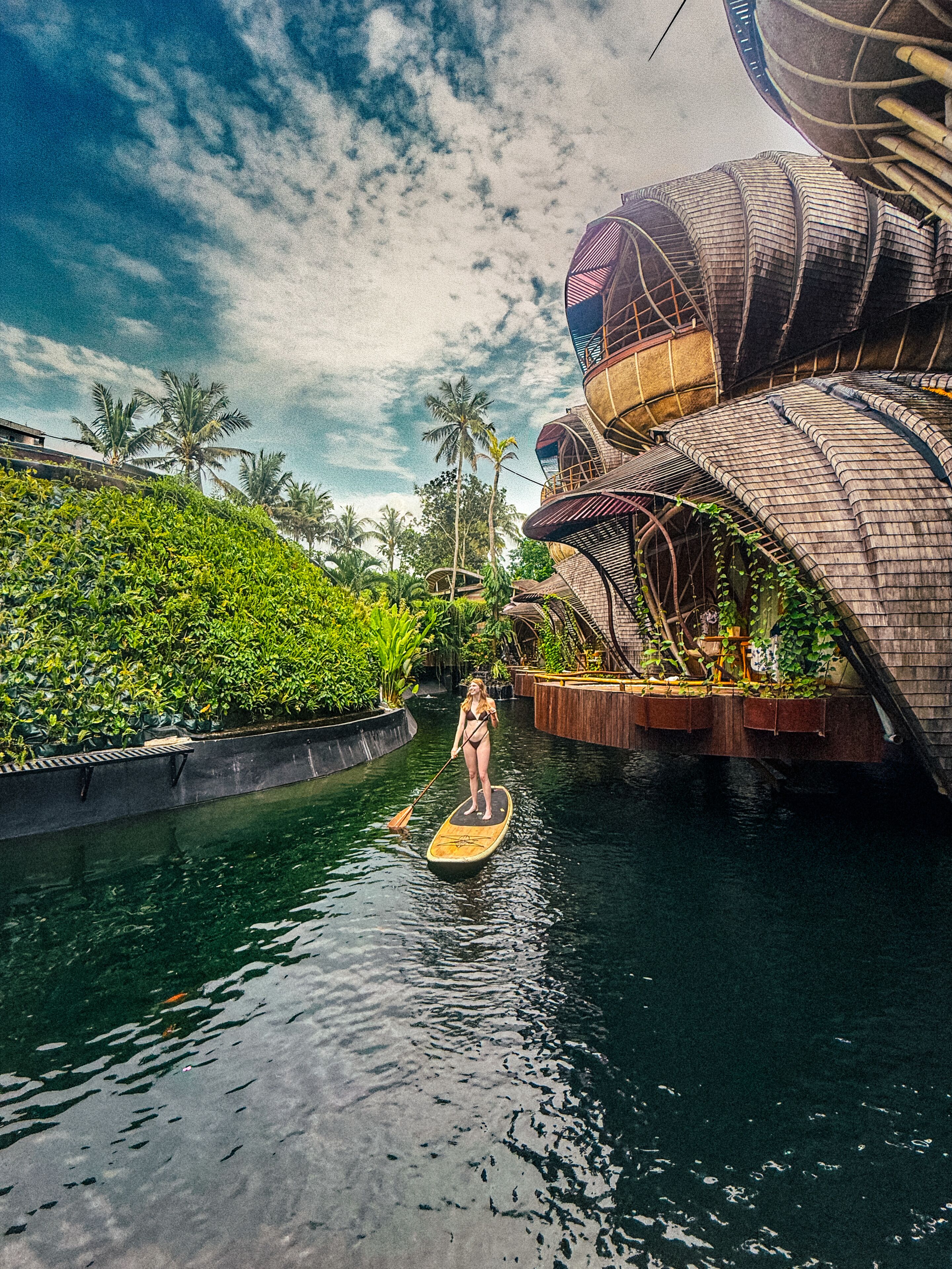 Una persona haciendo paddleboard en un canal con un edificio moderno a un lado.