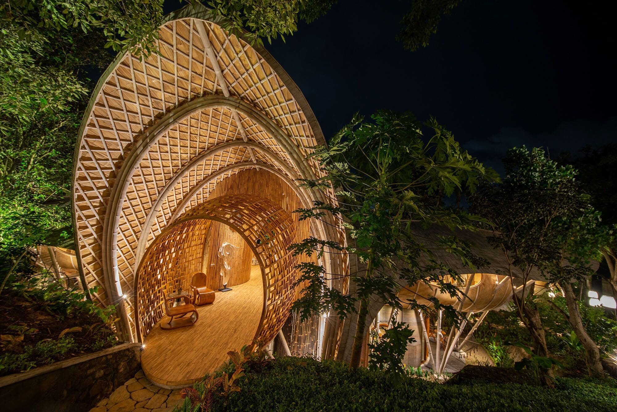 Una casa en el árbol con exterior de madera curvada y techo de paja, rodeada de abundante vegetación.