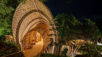 Una casa en el árbol con exterior de madera curvada y techo de paja, rodeada de abundante vegetación.