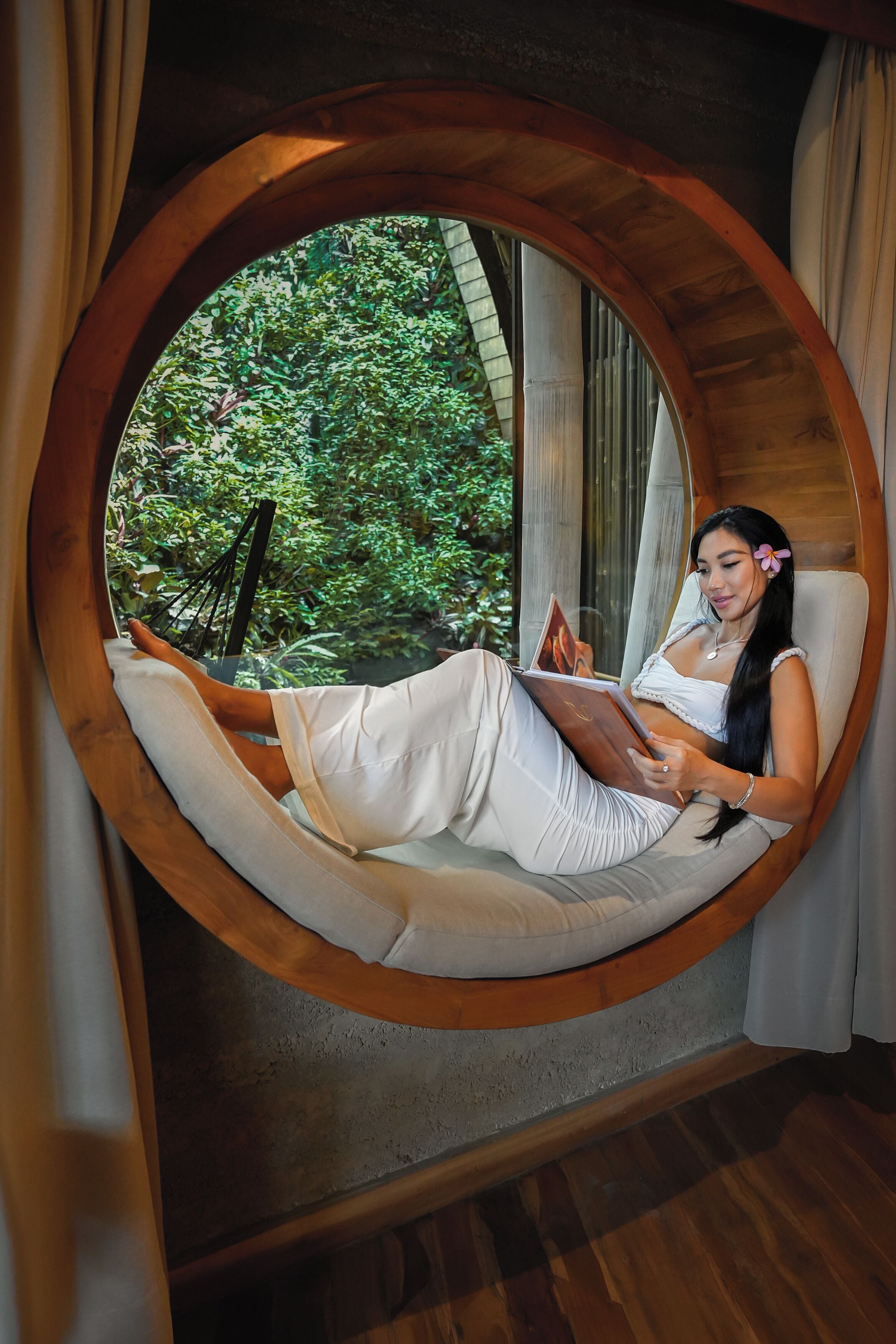 A circular wooden window with a person reclining inside, reading a book.