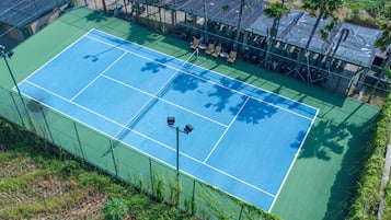 A tennis court with a surrounding fence, seating area, and palm trees.