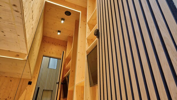 Un interior de madera con techo inclinado, estanterías empotradas y una puerta que da a otra habitación.