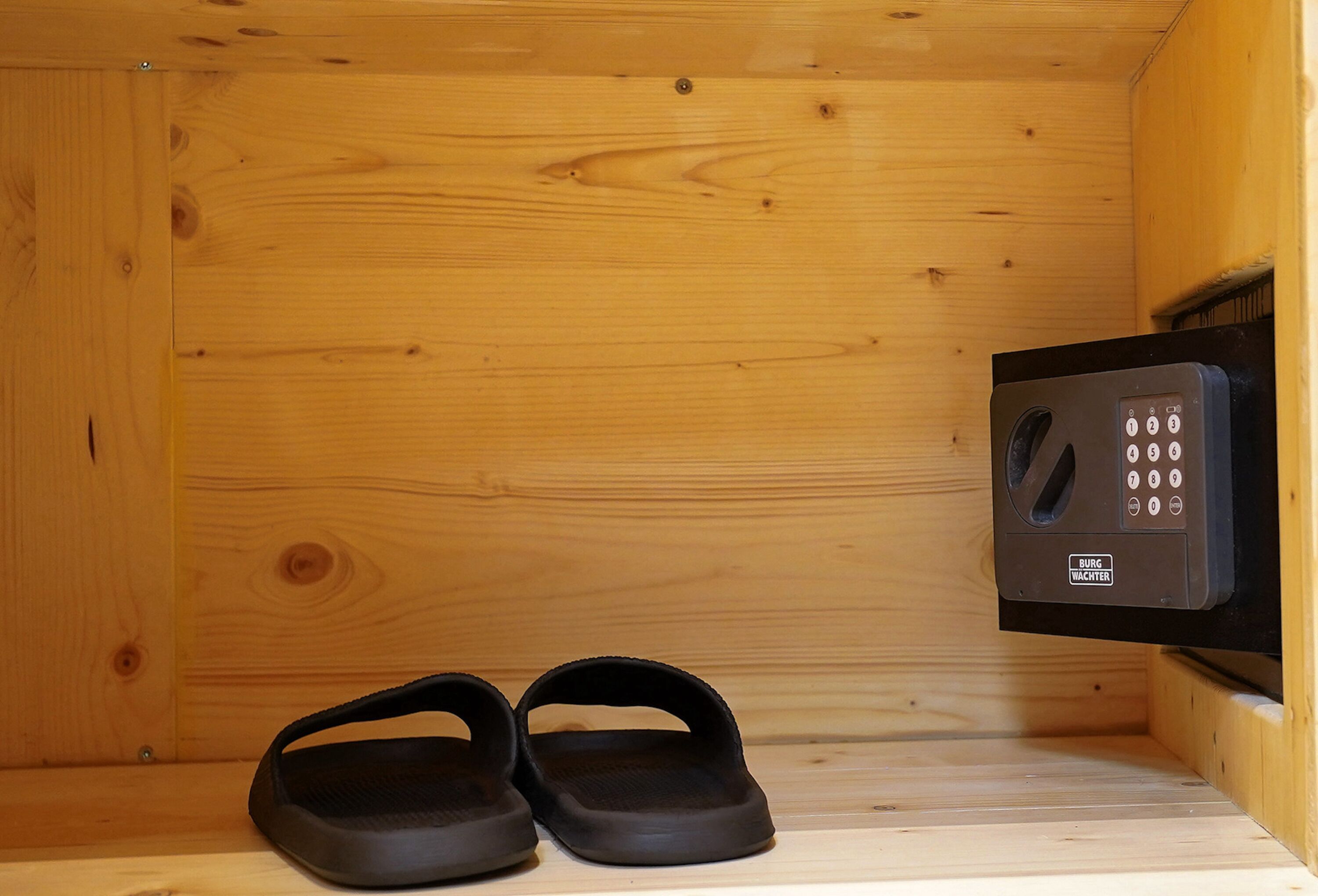 A wooden cabin interior with a sauna, a control panel, and a pair of black slippers on the floor.