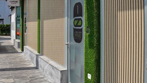 Entrada de hotel con diseño moderno, que incluye un puerta de vidrio con un logotipo, un jardín vertical verde y un letrero que dice 'Ljubljana Capsule Hotel'.