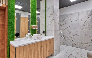 Un baño moderno con pared de mármol blanco, tocador de madera y jardín vertical verde.