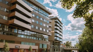 Un immeuble moderne à plusieurs étages, doté de balcons, avec une rivière au premier plan et un pont en arrière-plan.