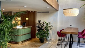 A modern interior with a wooden reception desk, a dining area with red chairs, and a hanging light fixture. - Via Sants Hotel Barcelona, Tapestry Collection by Hilton (Barcelona)