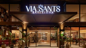The entrance of Via Sants Barcelona with a modern design, featuring a well-lit facade, potted plants, and a reception area visible through the glass doors. - Via Sants Hotel Barcelona, Tapestry Collection by Hilton (Barcelona)