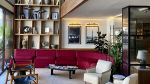 A spacious living area with a red sofa, two armchairs, a coffee table, and a bookshelf filled with decorative items. - Via Sants Hotel Barcelona, Tapestry Collection by Hilton (Barcelona)