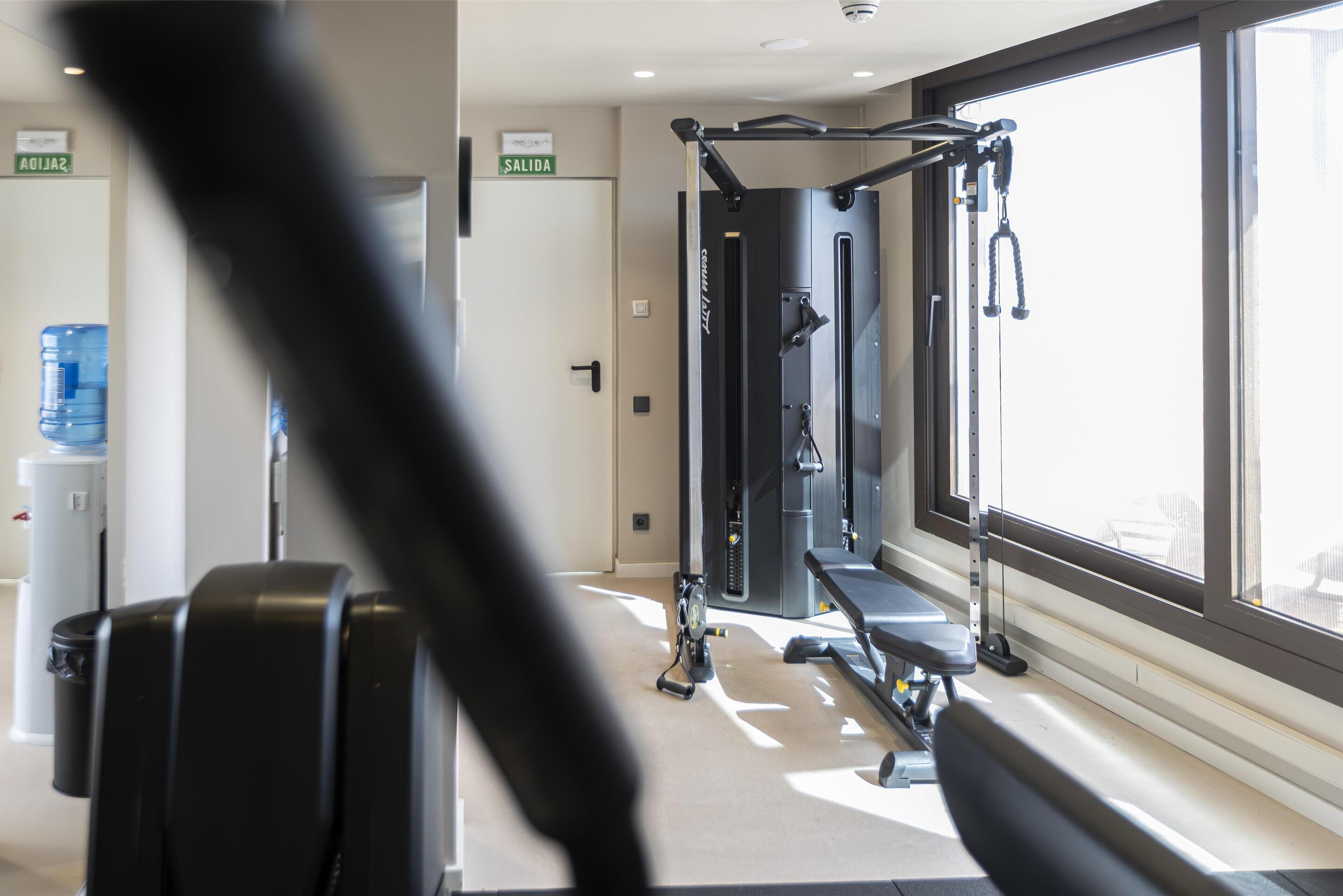 Un gimnasio con equipamiento de ejercicio, un dispensador de agua y un letrero que indica la salida.