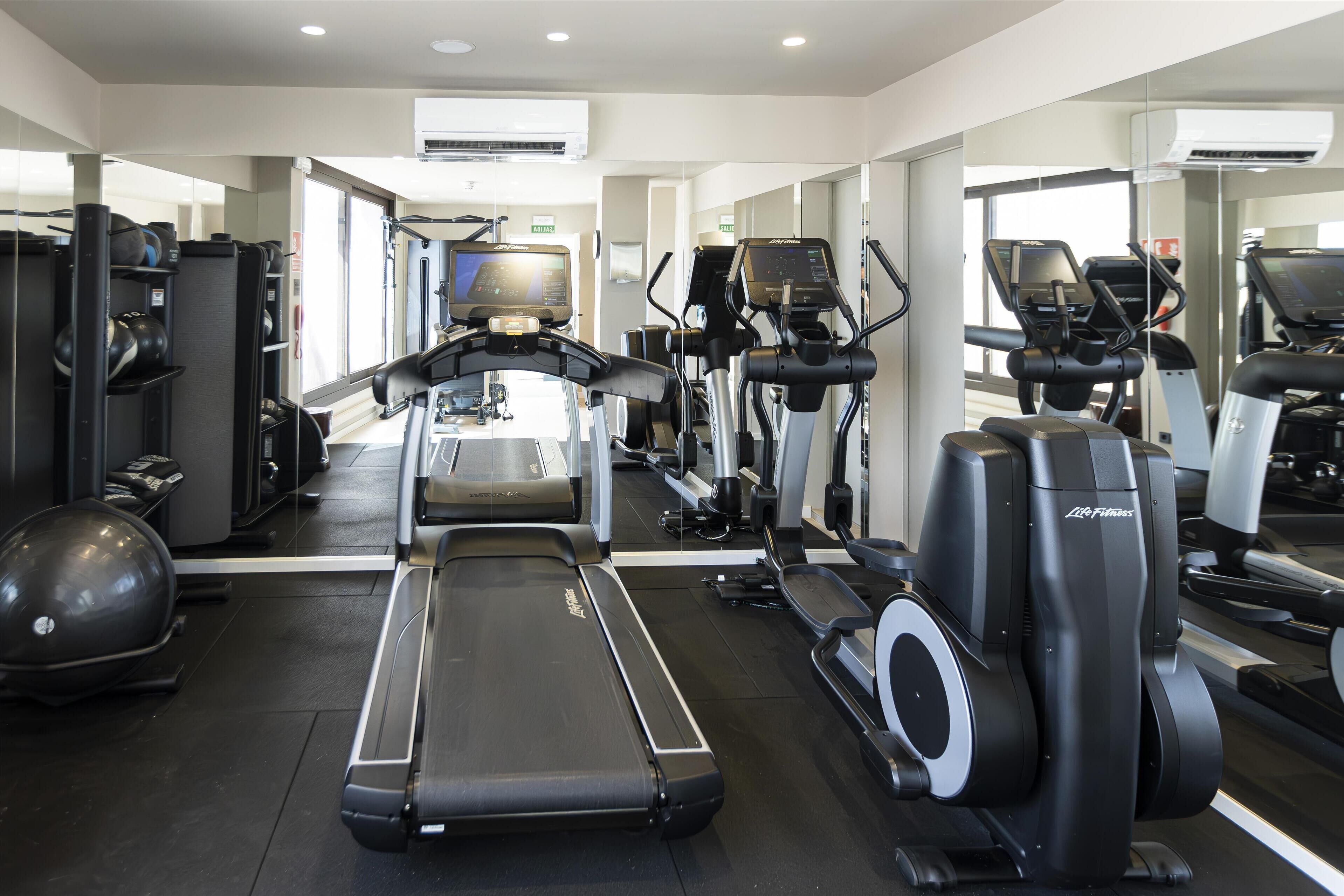 A gym with treadmills, elliptical machines, and exercise balls.