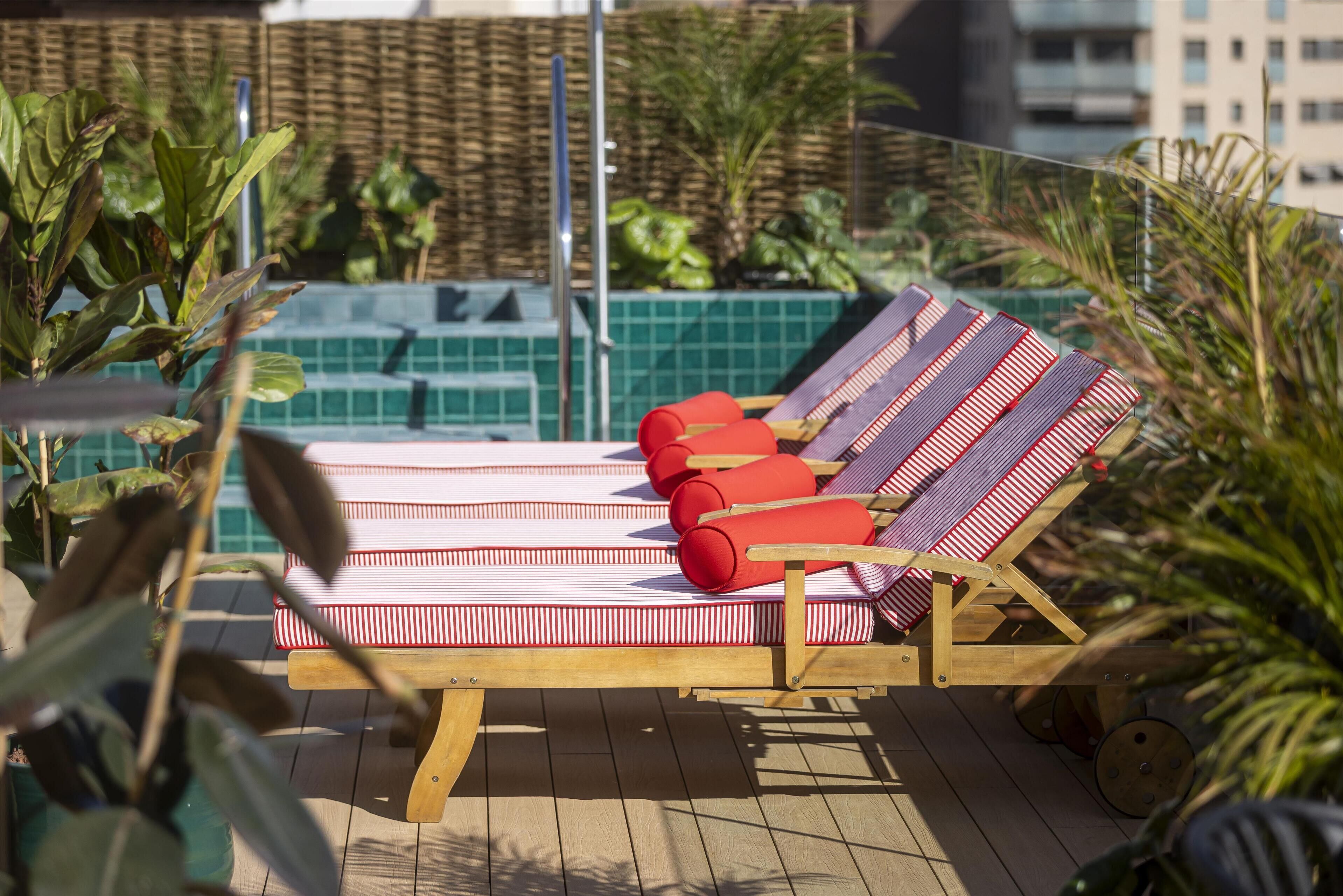 Una tumbona con cojines rojos sobre una terraza de madera, con un muro de azulejos verdes al fondo.
