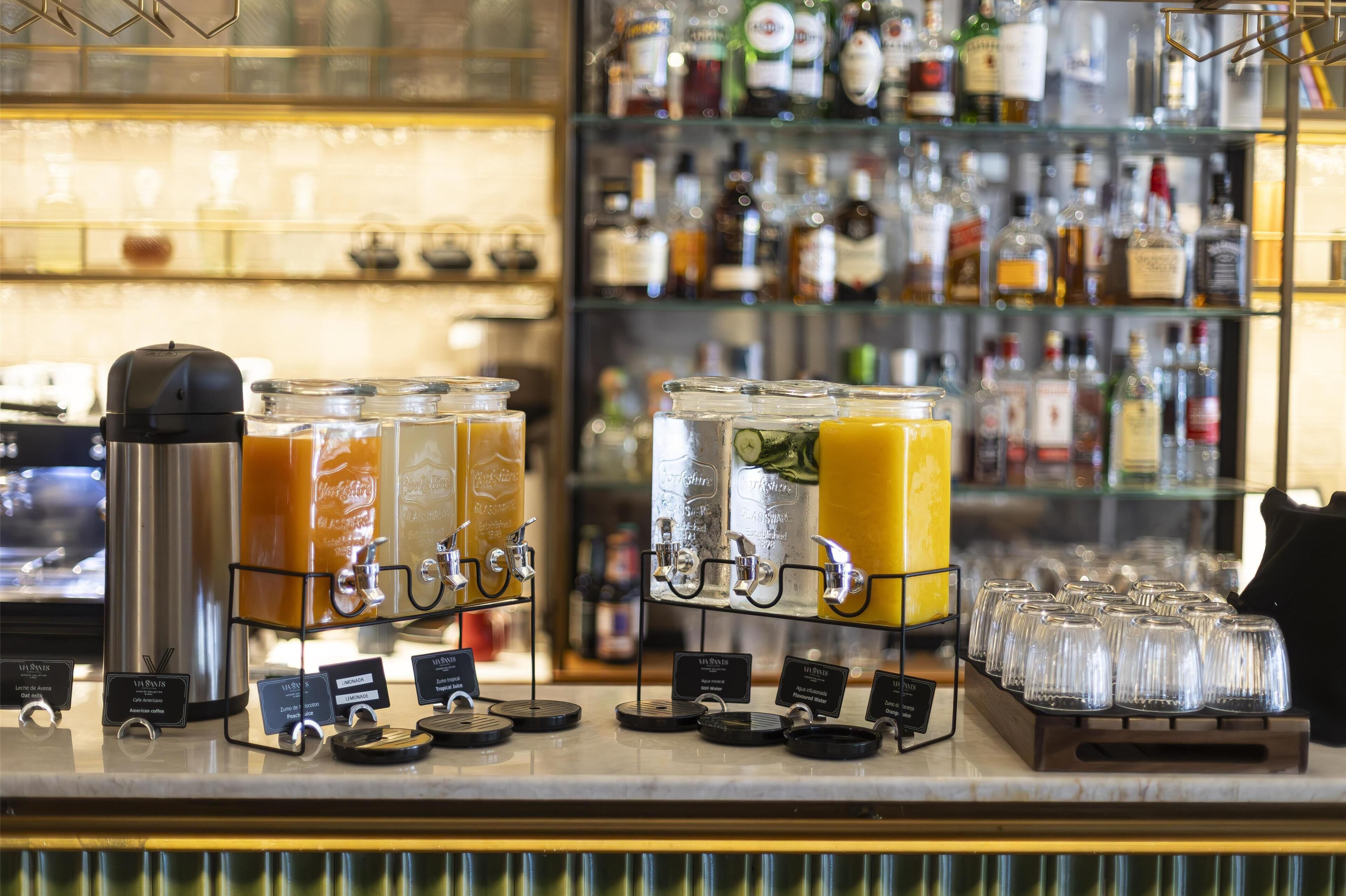 Zona de bar con varios dispensadores de bebidas y una vitrina llena de diferentes botellas.