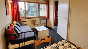 A compact room with a bed, a small table, a chair, and a window with curtains.