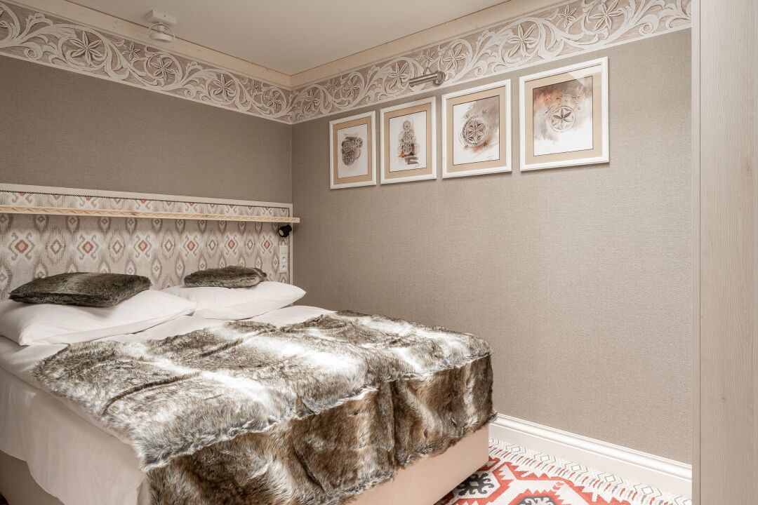 A bedroom with a bed, patterned headboard, decorative wall paneling, and framed artwork.
