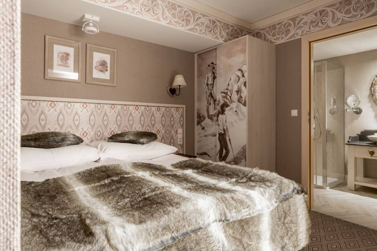 Une chambre d’hôtel avec une tête de lit à motifs, un grand lit recouvert d’un plaid en fausse fourrure, une lampe fixée au mur et un miroir doté d’un cadre décoratif.