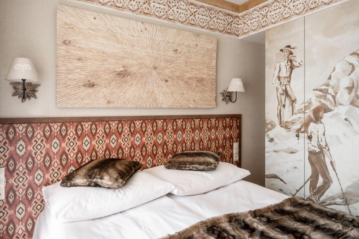 Un lit avec une tête de lit à motifs, deux lampes fixées au mur et une grande œuvre d’art abstraite au-dessus du lit.