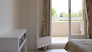 Una stanza con un letto, un tavolo bianco e una porta scorrevole in vetro che dà su un balcone.