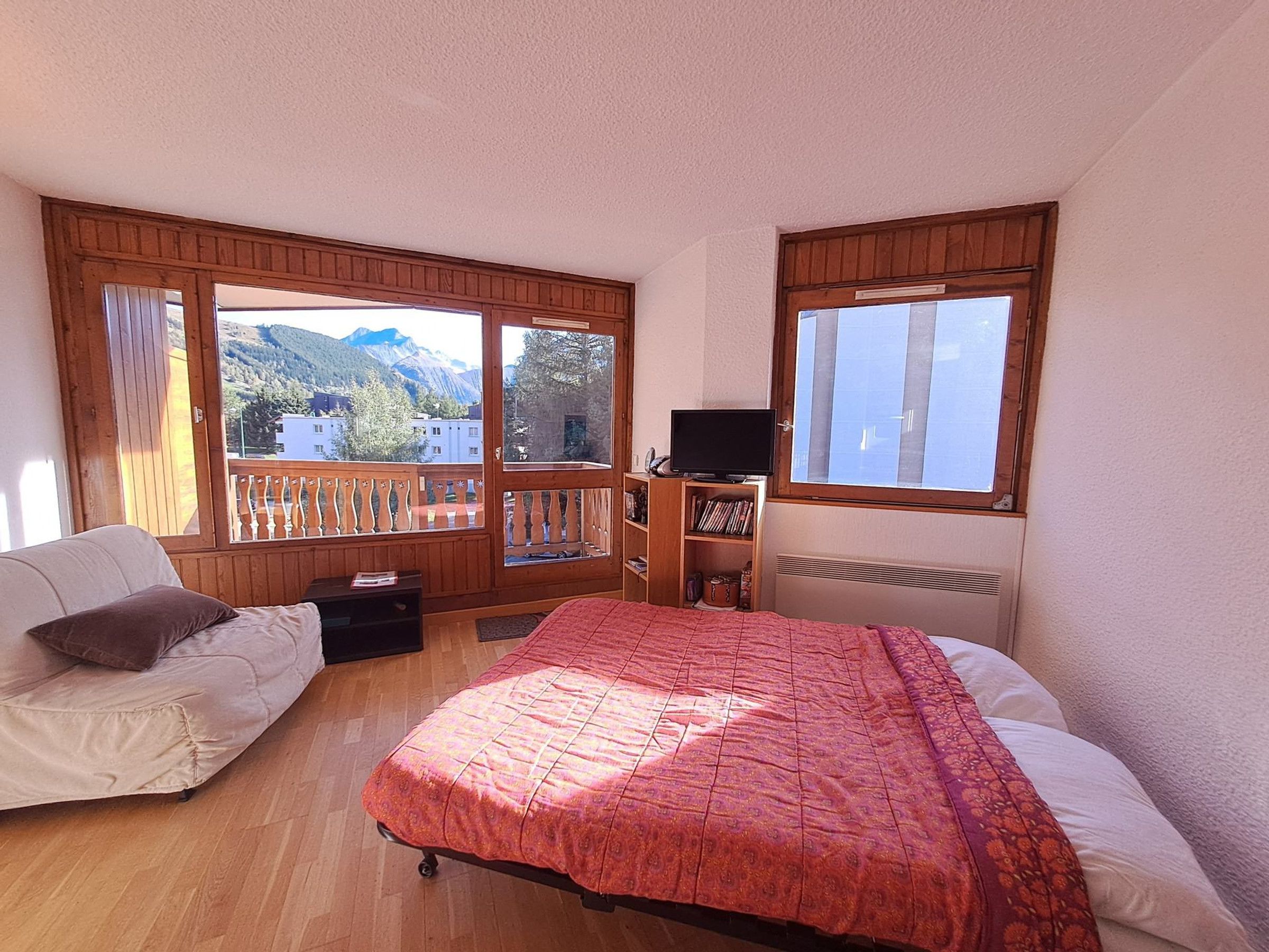 Un dormitorio con cama, sofá, televisión y ventana con vistas a montañas.