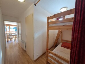 A room with a bunk bed, a dining area with chairs and a table, and a door leading to another room.
