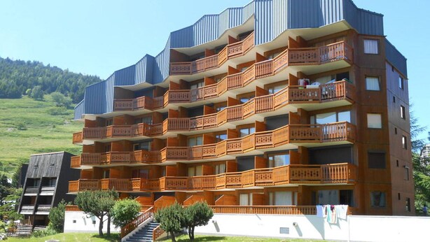 Un hôtel à plusieurs étages doté de balcons, d’un escalier et d’une pelouse devant l’entrée.