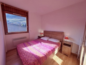Une chambre à coucher avec un lit, deux tables de chevet, une fenêtre et un radiateur.