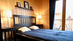 A bedroom with a wooden headboard, two bedside tables with lamps, a bed with a blue bedspread, and a view of a wooden deck outside.