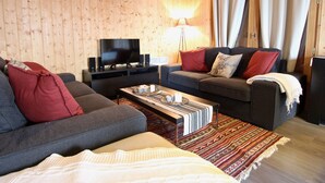 A cozy living room with a wooden wall, a sofa, a coffee table, and a TV.