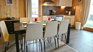 A wooden interior with a dining table set for four, a kitchen area with modern appliances, and a window with curtains.