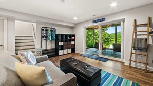 Ein modernes Wohnzimmer mit einer Couch, einem Hocker und einer Schiebetür zu einer Terrasse mit Seeblick und viel Grün.