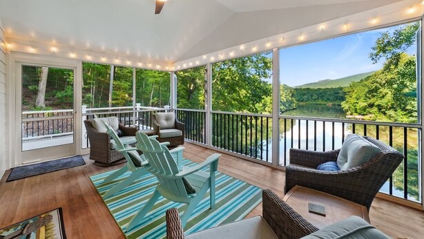 Ein überdachter Außenbereich mit Korbmöbeln, einem Deckenventilator und Blick auf einen See und Wald.