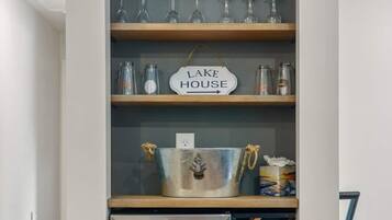 A kitchen area with a built-in wine cooler, shelves with glassware, and a sign that reads "LAKE HOUSE".