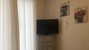 Quarto com televisão sobre um armário de madeira, parede branca e duas molduras.